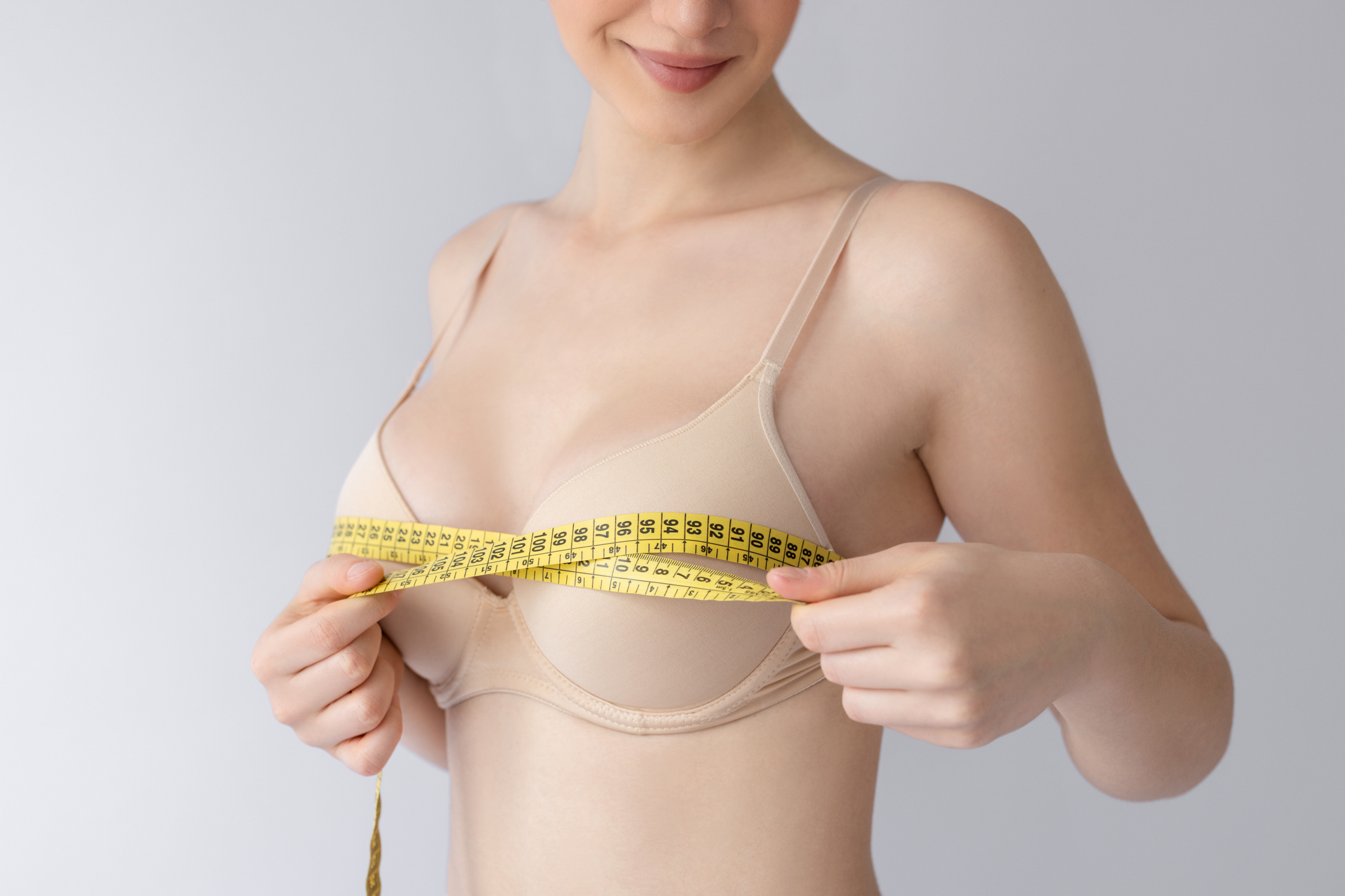 Woman measuring her bust with a tape measure after breast reduction with liposuction.